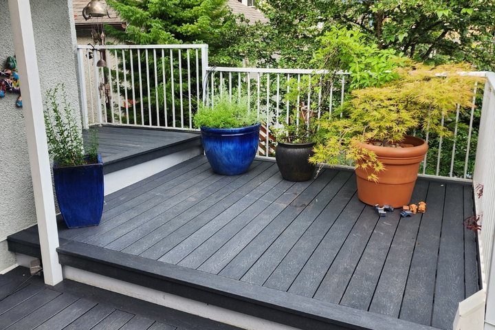 A backyard deck laid in dark grey recycled plastic lumber with potted plants along the rail