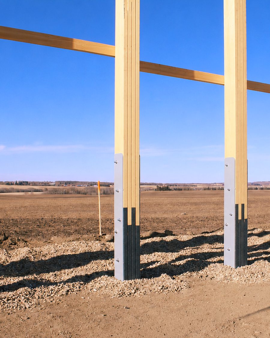 A row of Eco Column recycled plastic post-frame foundations carrying the timber posts of a new post-frame building on an Alberta field