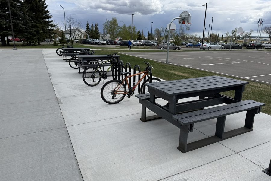 Recycled plastic picnic tables beside bike racks and a basketball court