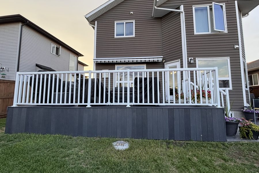 A raised backyard deck with white railings and dark recycled plastic skirting
