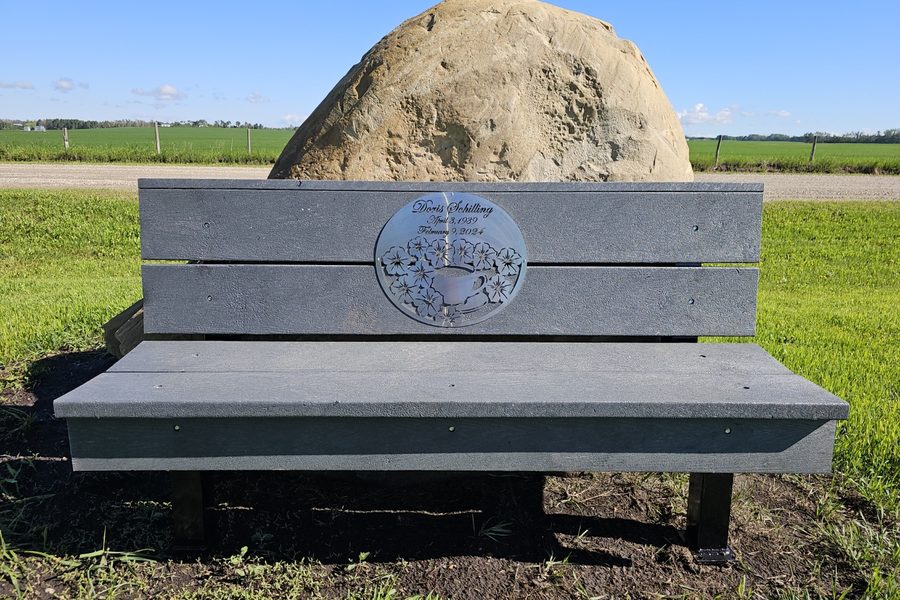 A recycled plastic memorial bench with an inset plaque, set beside a boulder