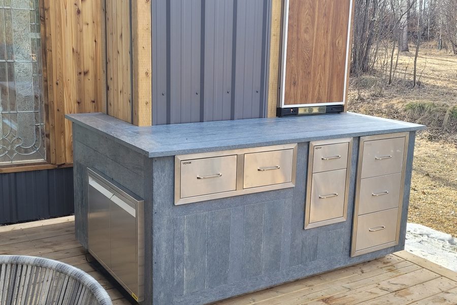An outdoor kitchen island clad in grey recycled plastic board around stainless drawers
