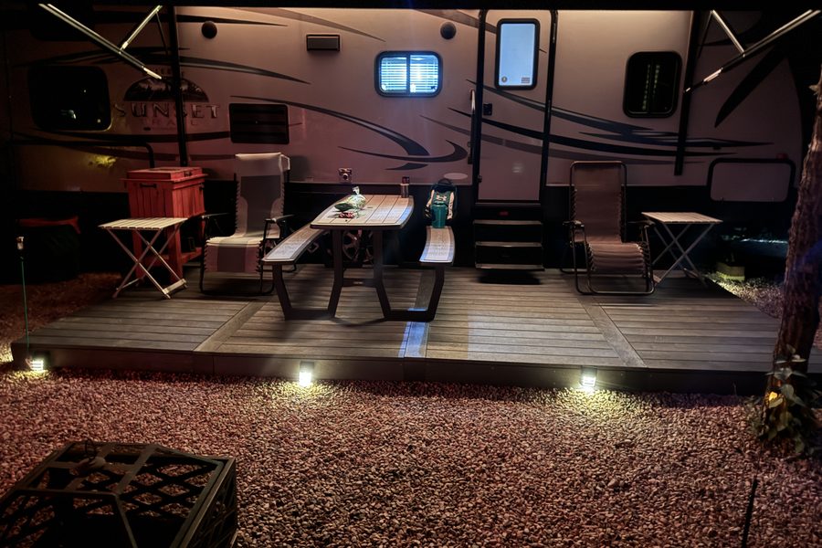 A lit recycled plastic deck pad beside a travel trailer, with a picnic table