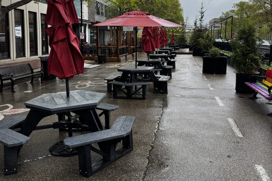 Recycled plastic picnic tables set down a closed street under red market umbrellas