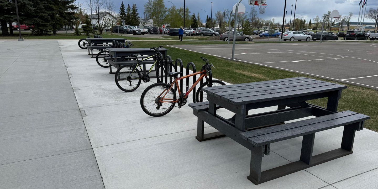 A recycled plastic picnic table beside bike racks in a public parking lot