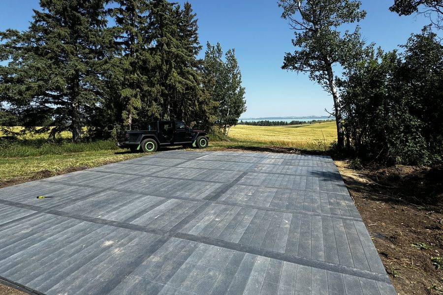 Recycled plastic board laid on bare ground on an Alberta acreage, with trees and open prairie beyond
